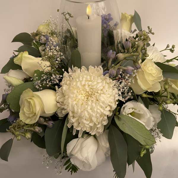 White floral arrangement around a glass candle holder with a lit candle