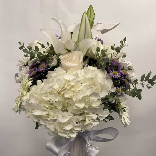 White floral arrangement in a ribbed vase with a silver ribbon