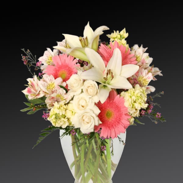 Pink gerberas, white lilies, and cream roses in a clear glass vase