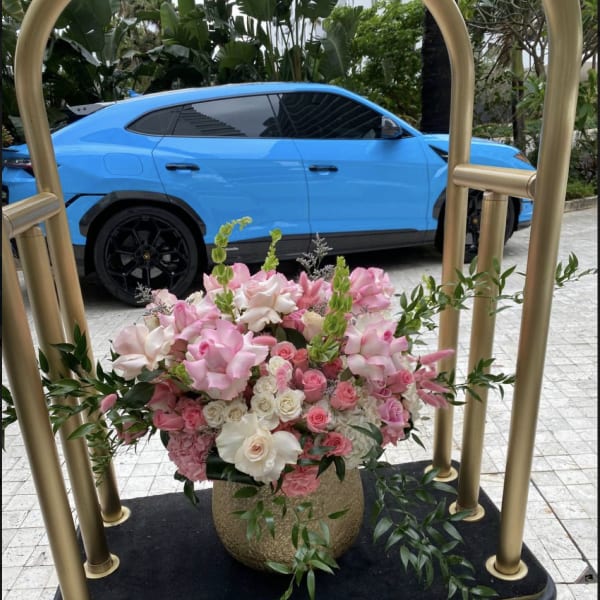 Pink and white floral arrangement in a gold vase on a cart