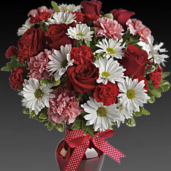 Red roses, white daisies, and pink carnations in a red vase with a polka-dot ribbon