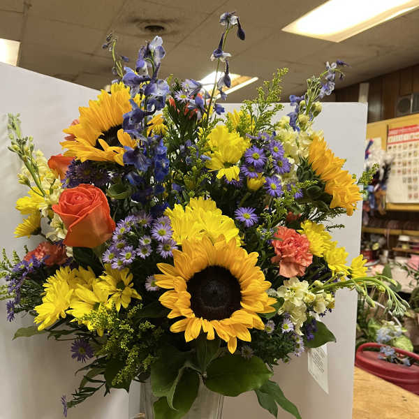Mixed bouquet with sunflowers, roses, and purple flowers in a tall vase