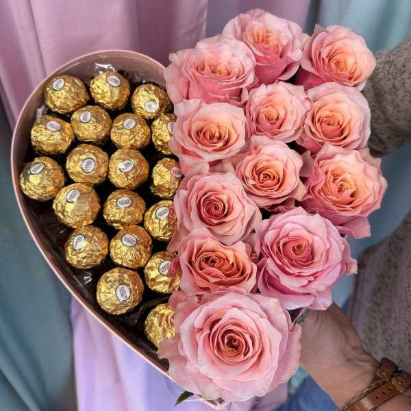 Pink roses arranged beside gold-wrapped chocolates in a heart-shaped box