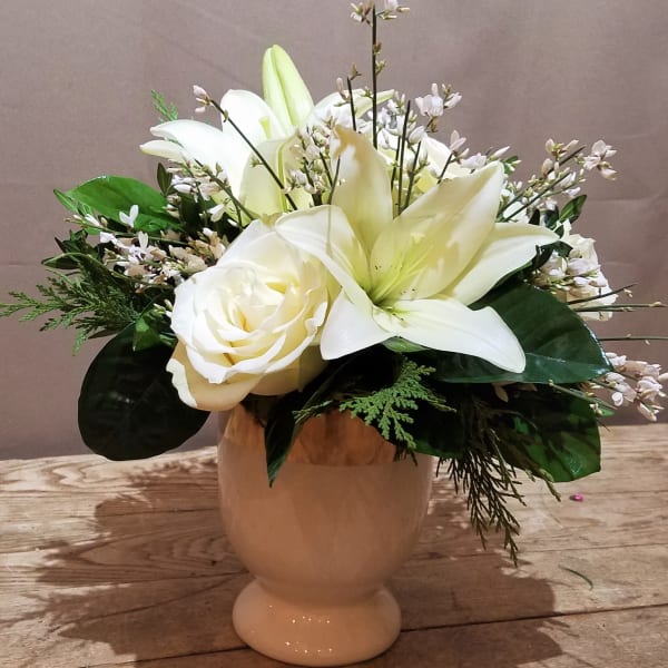 White lilies and roses in a cream pedestal vase on a wooden surface