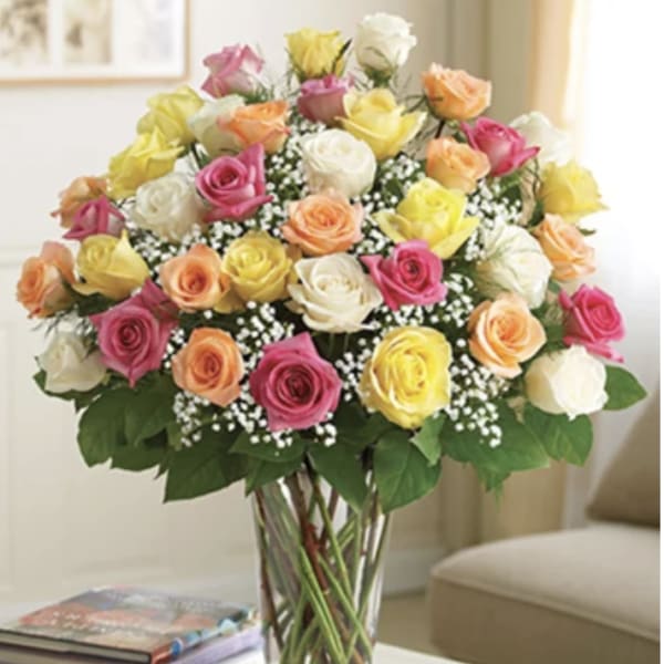 Mixed roses in pink, yellow, peach, and white in a clear glass vase