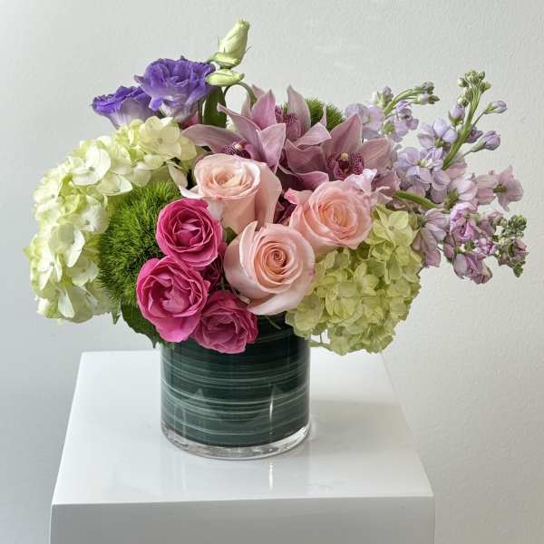 Mixed pink, purple, and green flowers arranged in a glass vase.