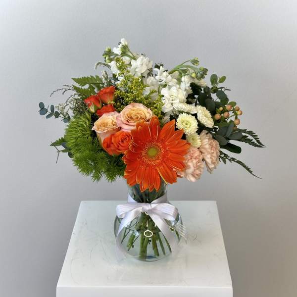 Mixed bouquet with orange gerbera daisies and roses in a glass vase