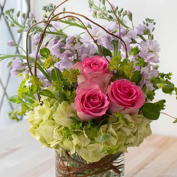 Pink roses and lavender flowers in a glass vase with curly branches