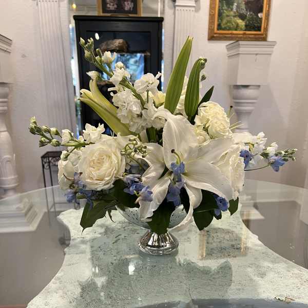 Low white and blue flower arrangement with lilies and roses in a silver pedestal vase