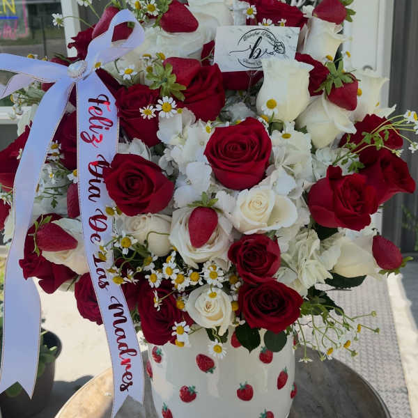 Bouquet of red and white roses in a strawberry-patterned vase with a ribbon