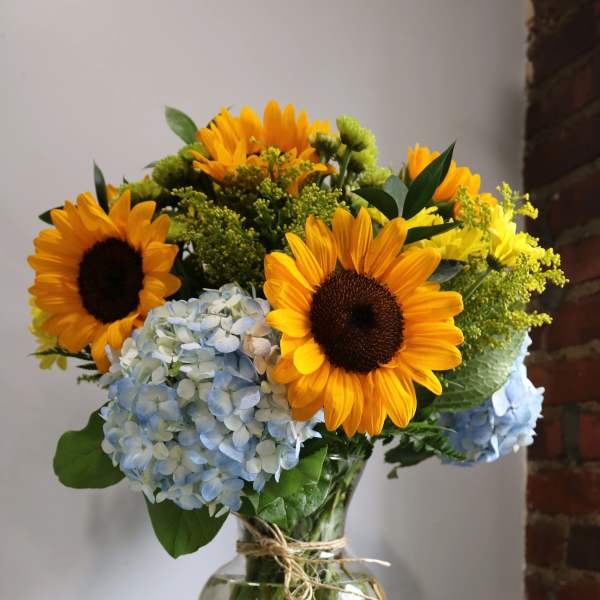 Sunflowers and blue hydrangeas arranged in a glass vase