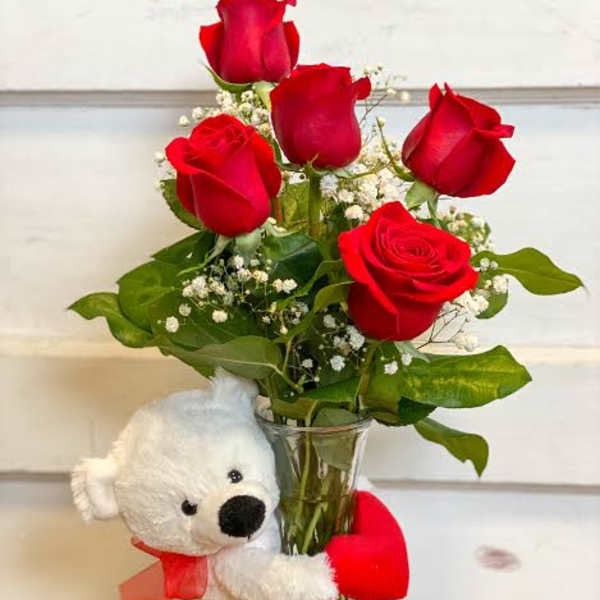 Red roses in a glass vase with a white teddy bear