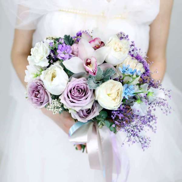 Bride holding a pastel bouquet of roses, orchids, and purple filler flowers