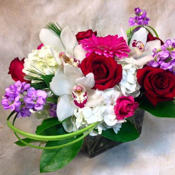 Bouquet of red roses, white orchids, and purple flowers in a glass vase