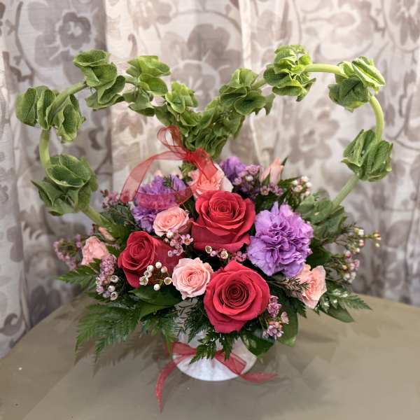 Heart-shaped floral arrangement with roses and purple carnations