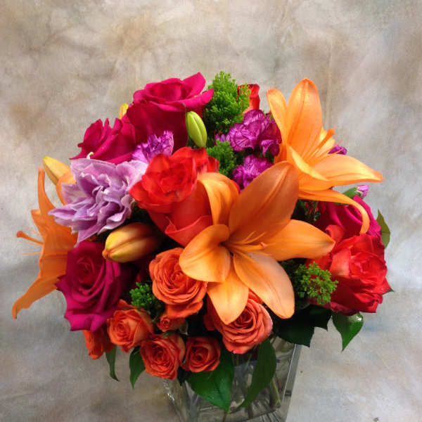 Bright mixed bouquet in a clear square vase with roses and lilies