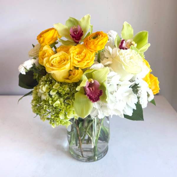 Yellow roses and white flowers in a clear glass vase