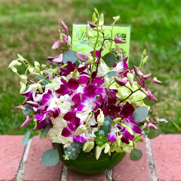 Purple and white orchid arrangement in a green glass bowl