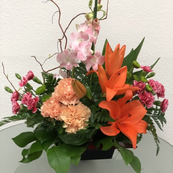 Orange lilies and pink carnations arranged in a low vase