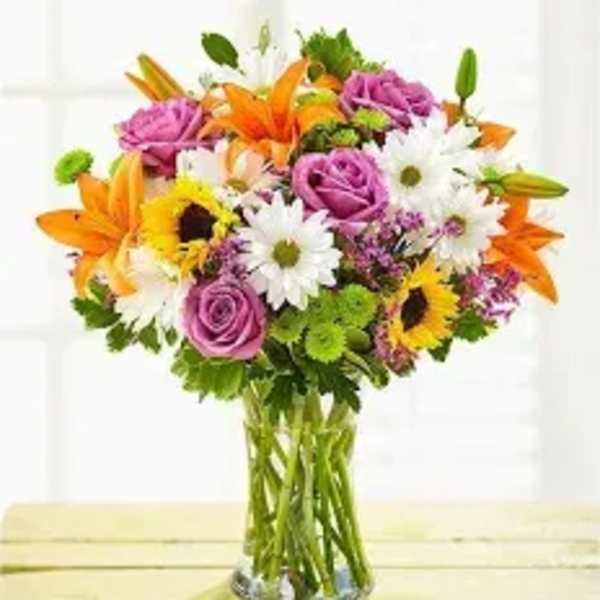 Mixed bouquet of orange lilies, purple roses, and white daisies in a glass vase
