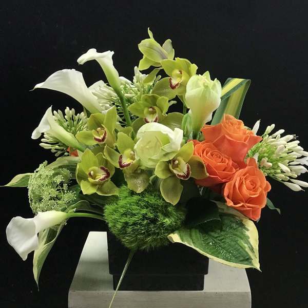 Arrangement of white calla lilies, green orchids, and orange roses in a black vase