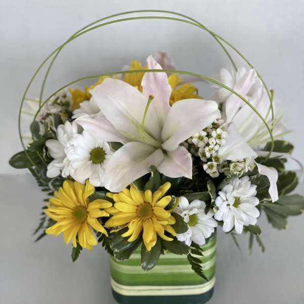 Mixed white and yellow flowers in a striped square vase with arched greenery