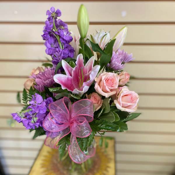 Bouquet of pink roses, purple flowers, and a pink lily with a ribbon