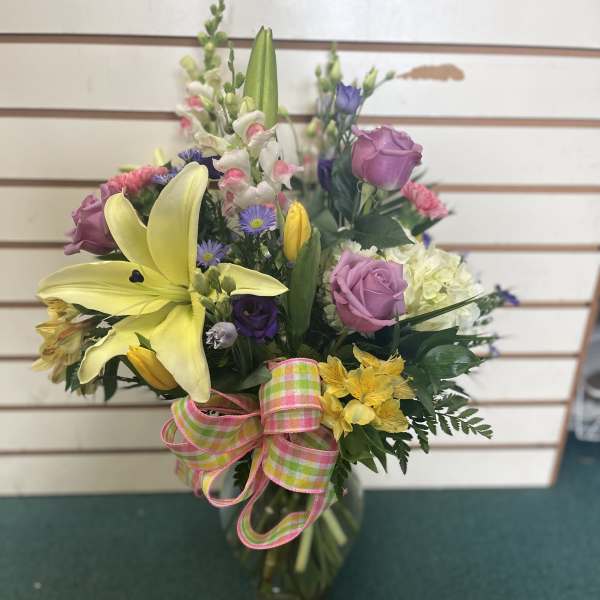 Mixed bouquet with yellow lilies, pink roses, and a plaid ribbon in a glass vase