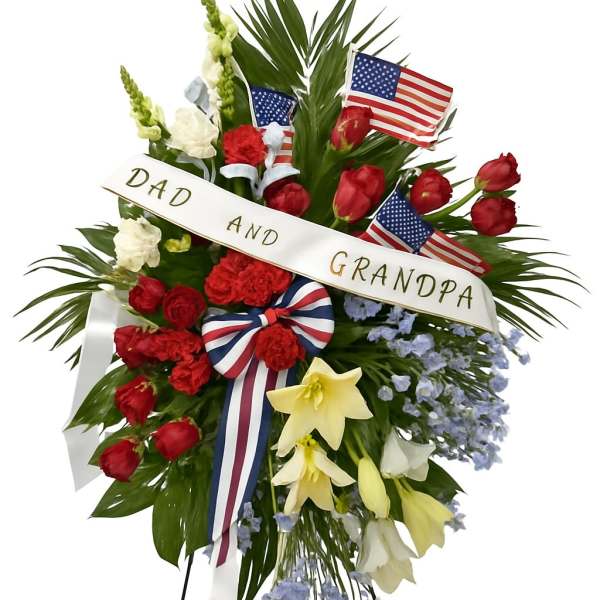 Standing floral tribute with red and white flowers, flags, and a memorial ribbon