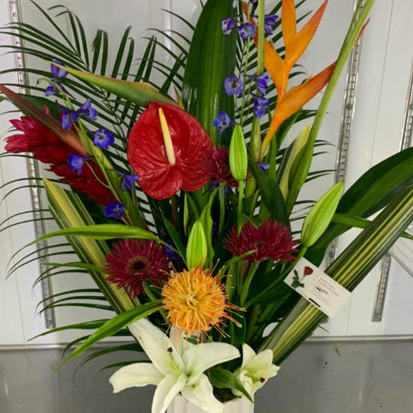 Tropical flower arrangement in a white vase with red, orange, purple, and white blooms