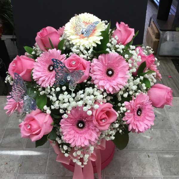 Pink roses and gerbera daisies in a pink box with butterfly picks