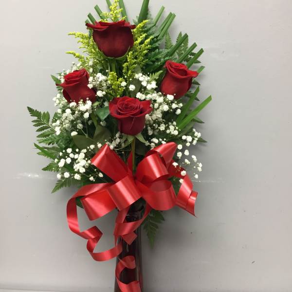 Red roses arranged in a tall vase with baby's breath and a red ribbon