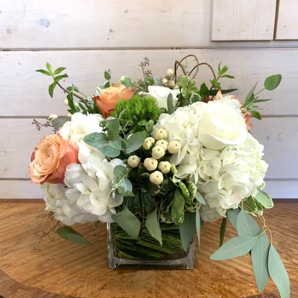 White hydrangeas and peach roses in a square glass vase