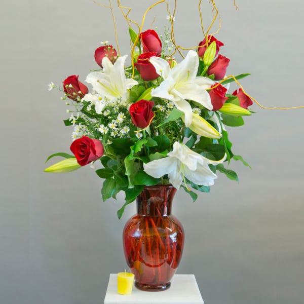 Red roses and white lilies in a red glass vase with a small yellow candle.