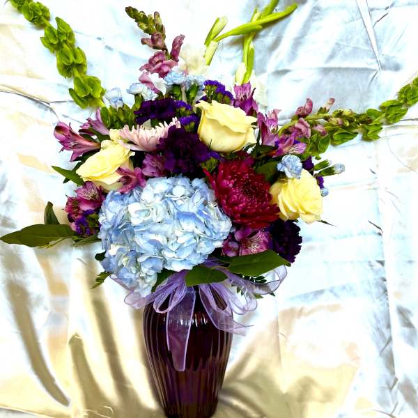 Mixed bouquet in a purple vase with blue hydrangea and yellow roses