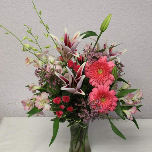 Mixed bouquet in a glass vase with pink gerbera daisies, lilies, and roses