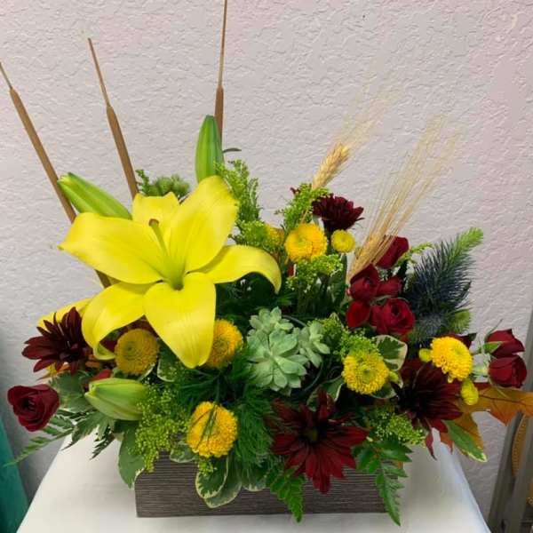 Yellow lilies and red roses in a rectangular vase with mixed accents