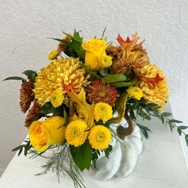 Yellow roses and chrysanthemums arranged in a white vase with autumn leaves