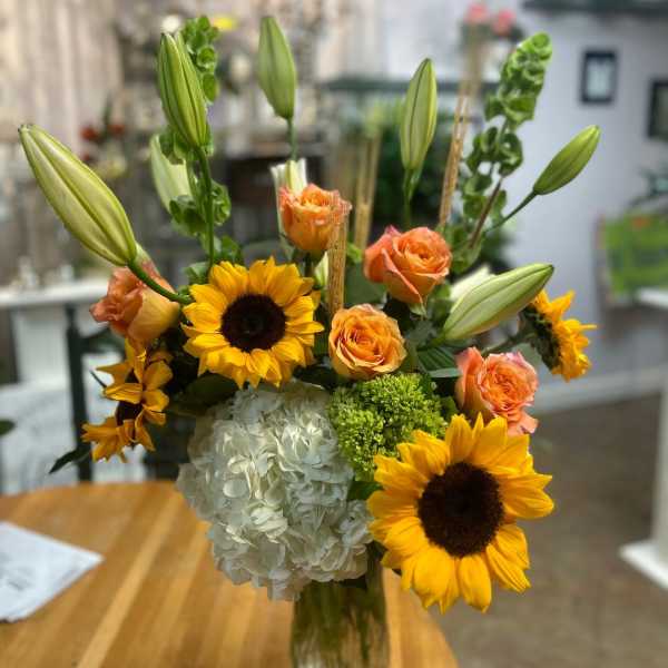 Bouquet of sunflowers, orange roses, lilies, and white hydrangea in a glass vase