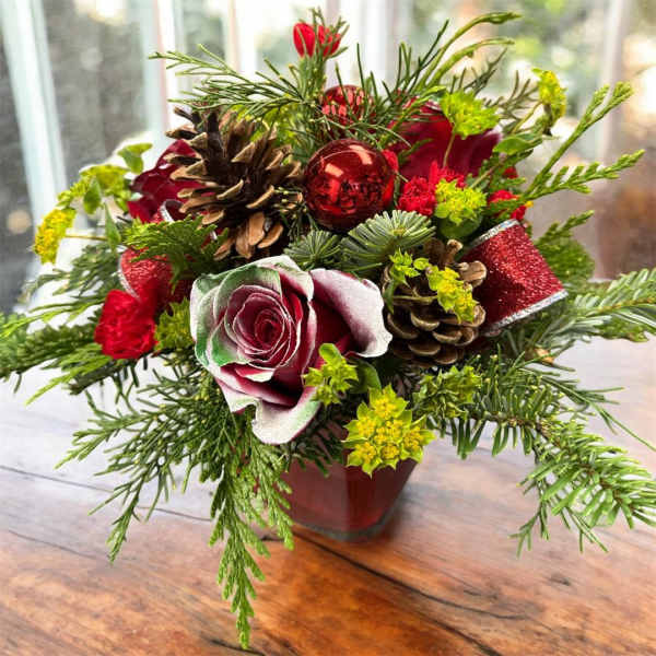 Holiday bouquet with red roses, pinecones, and a red ornament in a vase