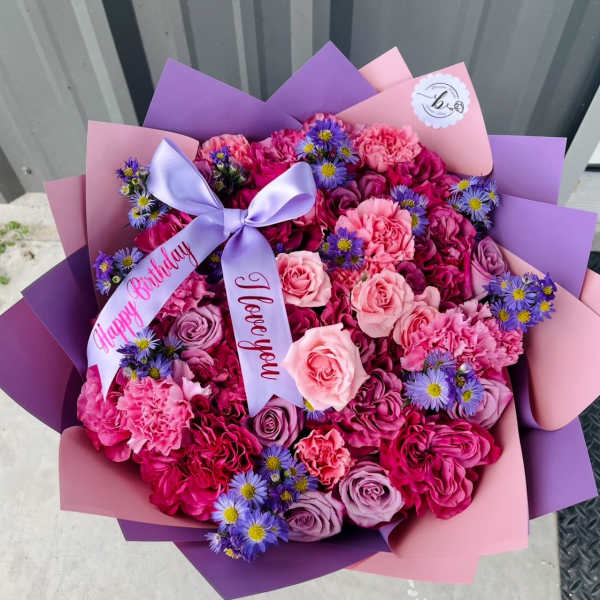 Pink and purple bouquet of roses, carnations, and small daisy-like flowers with ribbon
