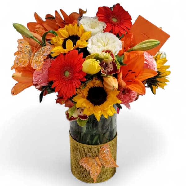 Bright mixed bouquet of sunflowers, lilies, and gerbera daisies in a glass vase with butterfly accents