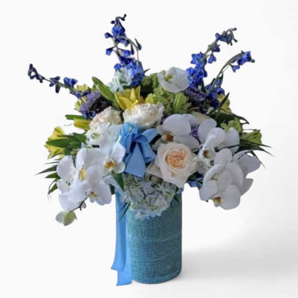 Tall bouquet of white orchids, cream roses, and blue flowers in a blue vase with a blue bow