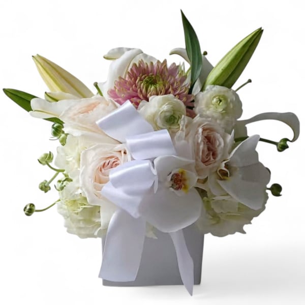 White and blush bouquet with lilies, roses, and a white ribbon in a gray vase