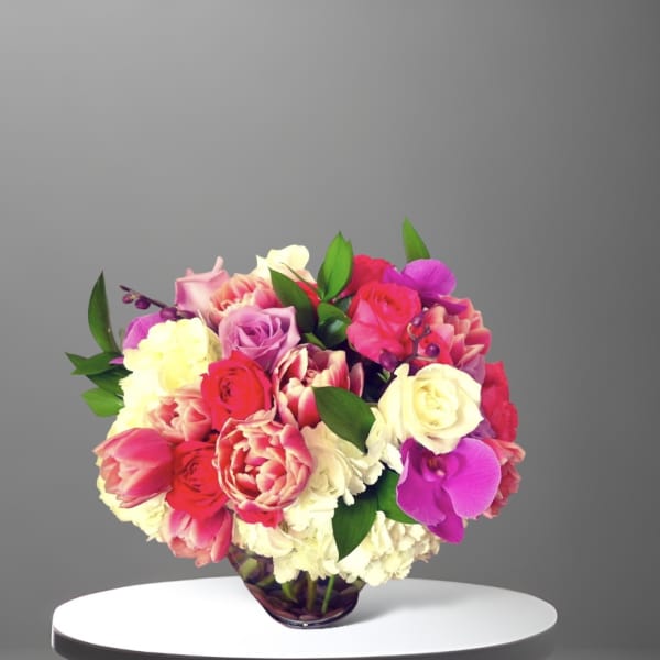 Mixed bouquet of roses, tulips, and orchids in a glass vase