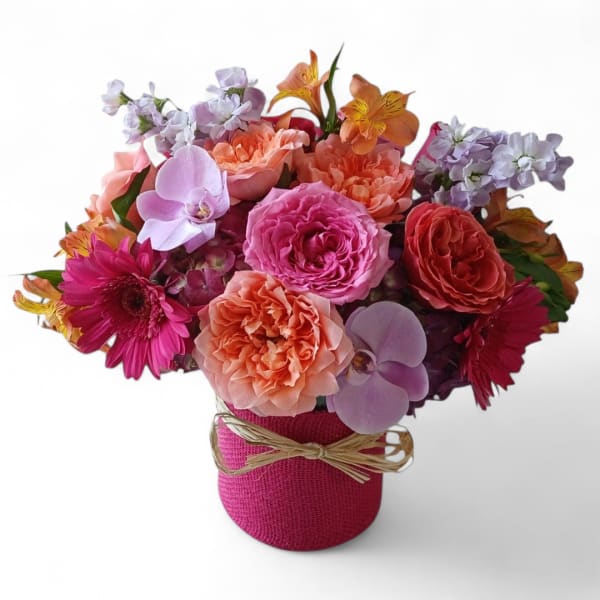Mixed bouquet of pink, peach, and lavender flowers in a pink wrapped vase