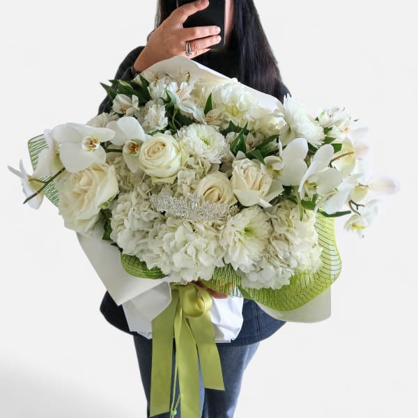 Large white bouquet of roses, hydrangeas, orchids, and mums with a tiara and green ribbon wrap