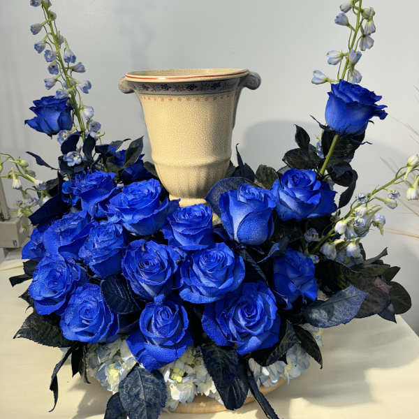 Blue roses arranged around a beige urn vase with tall blue flower spikes