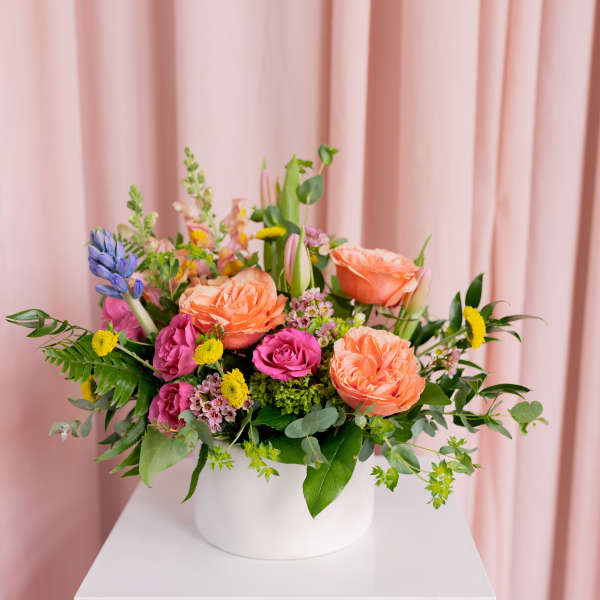 Mixed bouquet of peach, pink, and yellow flowers in a white vase