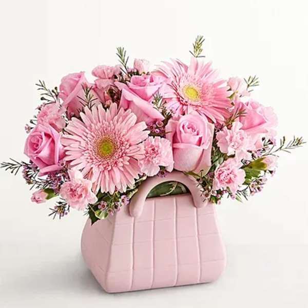 Pink roses and gerbera daisies in a pink handbag-shaped container